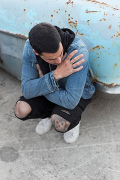 Young man crouching in front of a rusty car