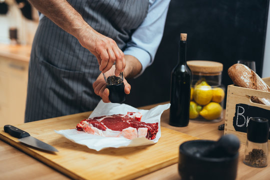 middle aged man preparing beef steak in his kitchen. seasoning the meat