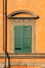 Closed baroque palazzo window with shutters on orange painted facade in Pisa, Italy