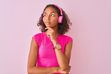 Young brazilian woman listening to music using headphones over isolated pink background serious...