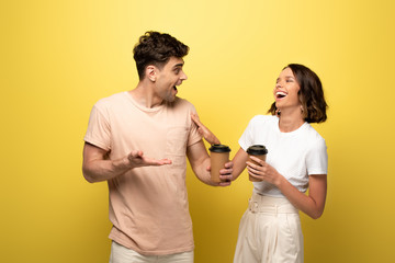 excited man and woman talking while holding coffee to go on yellow background