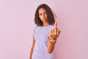 Young brazilian woman wearing t-shirt standing over isolated pink background Showing middle finger,...
