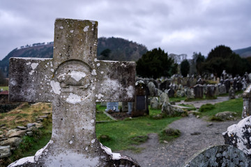 Fototapeta na wymiar Old catholic granite cross on tombstone with cemetery and tombstones in background, Glendalough, Ireland