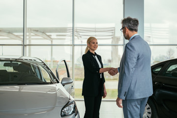 car sell agent handshake with customer in car showroom