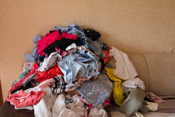 Front view of colorful childish clothes scattered on sofa at home. Big bunch of clothes lying at...