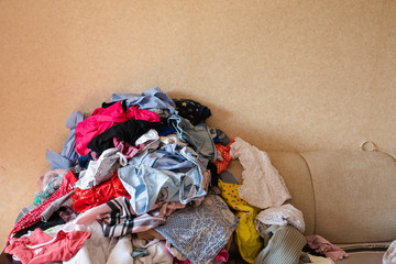 Front view of colorful childish clothes scattered on sofa at home. Big bunch of clothes lying at...