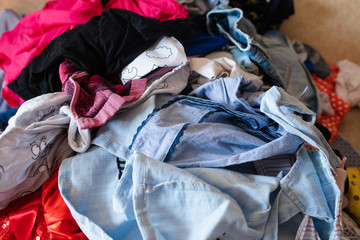 Front view of colorful childish clothes scattered on sofa at home. Big bunch of clothes lying at room before laundry. Concept of cleaning, mess, mud and household chores.