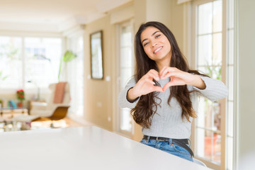 Young beautiful woman at home smiling in love showing heart symbol and shape with hands. Romantic...