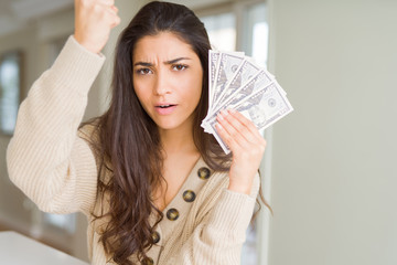 Young woman holding 50 dollars bank notes annoyed and frustrated shouting with anger, crazy and yelling with raised hand, anger concept