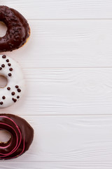 Three donuts on white wood with text space. Row of donuts on wood table. Top view and copy space.