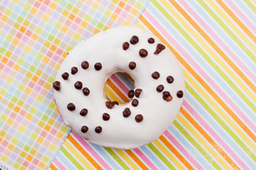 Donut on colored paper background. White glazed donut with chocolate crunchies. Freshly baked snack.