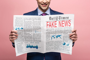 cropped view of businessman reading newspaper with fake news isolated on pink