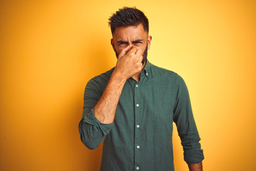 Young indian businessman wearing elegant shirt standing over isolated white background smelling something stinky and disgusting, intolerable smell, holding breath with fingers on nose. 