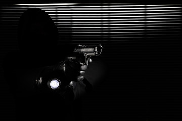 burglary and robbery. skillful professional masked burglar holding a gun and torch and breaking into the house, hand close up on black window background