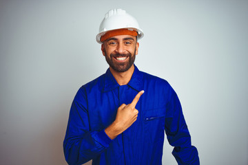 Handsome indian worker man wearing uniform and helmet over isolated white background cheerful with a smile of face pointing with hand and finger up to the side with happy and natural expression 