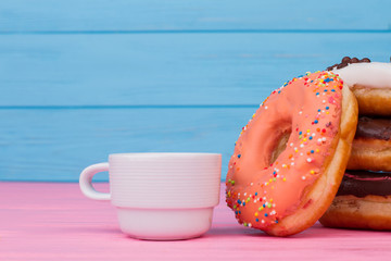 Donuts with sprinkles and cup of coffee on wood table. Glazed sweets on color background.