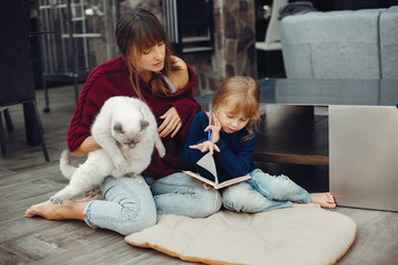 Beautiful mother with little daughter. Family sitting in the room. Cute girl doing homework. Woman playing with kitty