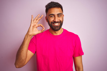 Young indian man wearing t-shirt standing over isolated pink background smiling positive doing ok...