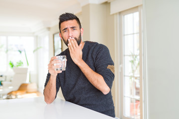 Handsome hispanic man drinking a fresh glass of water cover mouth with hand shocked with shame for mistake, expression of fear, scared in silence, secret concept