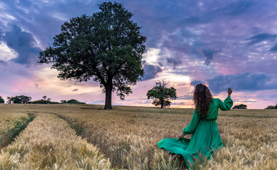 Portrait of a beautiful young woman in green dress on meadow watching the sunset enjoying nature