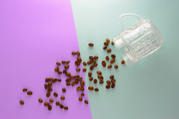 Coffee beans scattered on a purple and blue background from a transparent cup