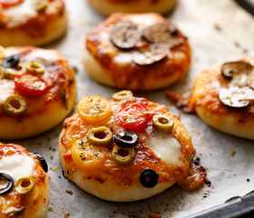 Small, vegetarian pizzas on white baking paper, close-up.