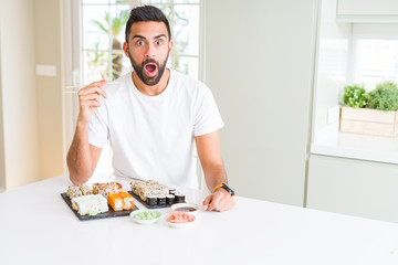 Handsome hispanic man eating asian sushi using chopsticks scared in shock with a surprise face, afraid and excited with fear expression