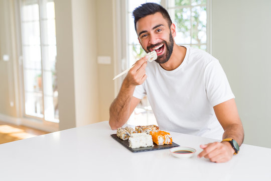 Handsome man smiling happy enjoying eating fresh colorful asian sushi using chopsticks