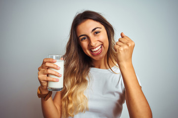 Young beautiful woman drinking a glass of milk over white isolated background screaming proud and celebrating victory and success very excited, cheering emotion