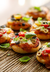 Small pizzas with the addition of cherry tomatoes, olives, mozzarella cheese and fresh basil on a rustic wooden background, close-up.