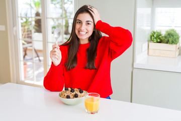 Beautiful young woman having healthy cereals and berries for breakfast stressed with hand on head, shocked with shame and surprise face, angry and frustrated. Fear and upset for mistake.