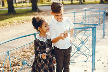 little beautiful dark-skinned girl walks in the autumn park with her European little friend