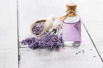 Glass bottle of Lavender essential oil with fresh lavender flowers and dried lavender seeds on white wooden rustic table, aromatherapy spa massage concept. Lavendula oleum