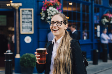 Young business lady in glasses standing by the pub with a pint of the beer.