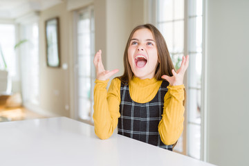 Beautiful young girl kid sitting on the table crazy and mad shouting and yelling with aggressive...
