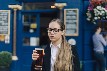 Young business lady in glasses standing by the pub with a pint of the beer.
