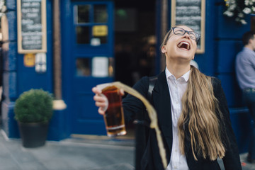 Young business lady in glasses standing by the pub with a pint of the beer.