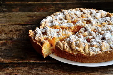 Slice of homemade apricot pie in a white plate on a wooden table.