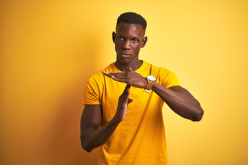 Young african american man wearing casual t-shirt standing over isolated yellow background Doing time out gesture with hands, frustrated and serious face