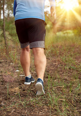 adult man in blue clothes and black shorts runs along the coniferous forest