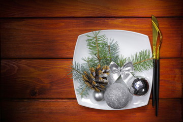 Christmas festive background. Christmas card with silver balls, pinecone and Christmas tree branch on the plate and cutlery. The concept of delicious and beautiful food for the winter holidays.
