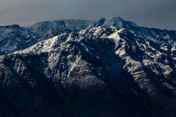 Fototapeta premium Cerro Ramon and Cerro La Cruz summits during a winter day. Snowcapped summits at central Andes mountains and amazing snowy rugged landscape on a cloudy day, an awe outdoor winter background scenery