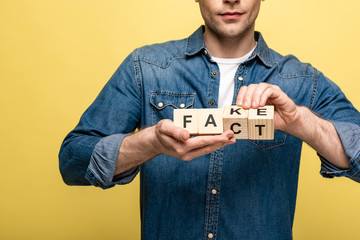 cropped view of man holding wooden cubes with fake fact lettering isolated on yellow