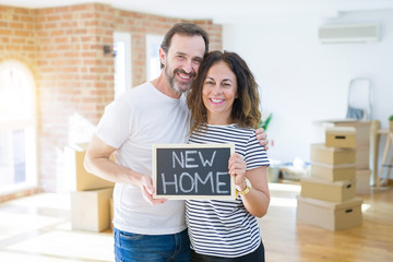 Middle age senior couple moving to a new house, smiling happy in love with apartmant holding a blackboard with new home text