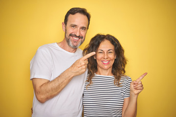 Naklejka premium Beautiful middle age couple together standing over isolated yellow background very happy pointing with hand and finger to the side