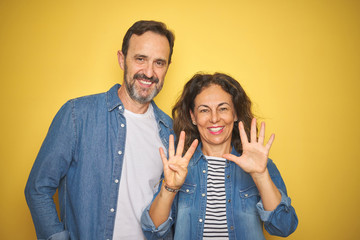 Beautiful middle age couple together wearing denim shirt over isolated yellow background showing and pointing up with fingers number nine while smiling confident and happy.