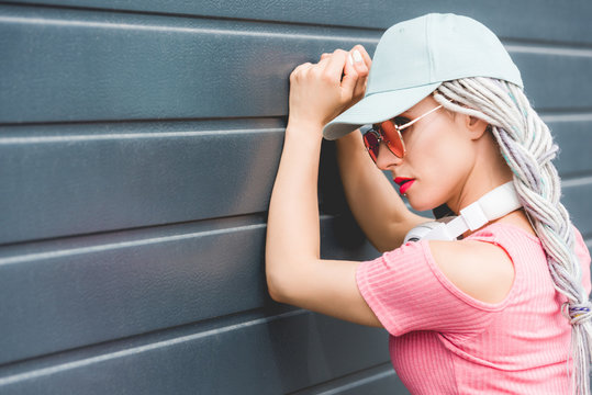 fashionable girl with dreadlocks and headphones leaning on wall