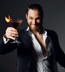 Stylish modern man bearded clubber in fashion suit looks skeptically at the glass with fresh...