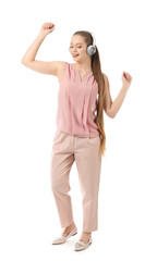 Beautiful young woman listening to music and dancing against white background