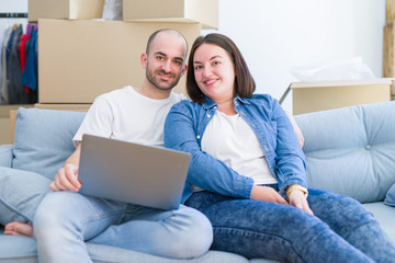 Fototapeta premium Young couple sitting on the sofa at new home using computer laptop, smiling happy for moving to a new apartment
